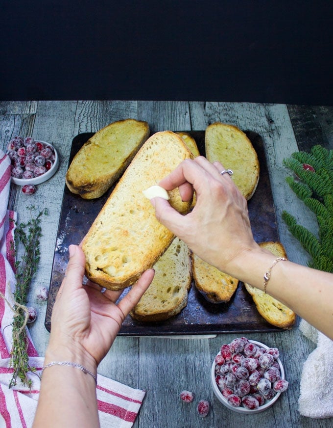 Two hands holding a piece of toasted bread and rubbing in a garlic clove into the bread for flavor