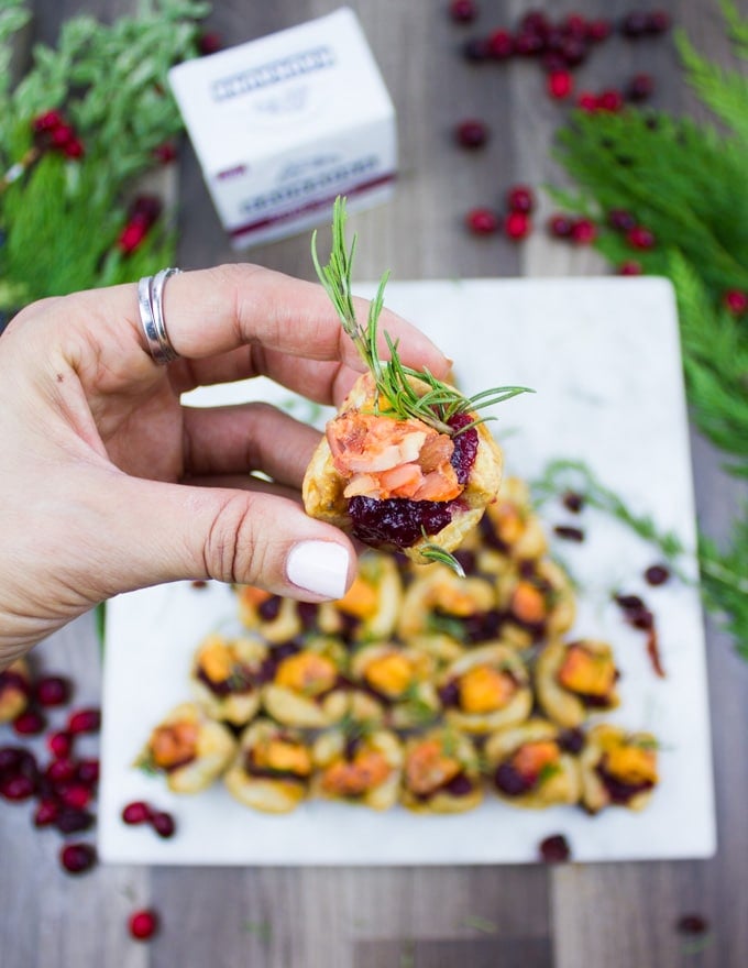 A hand holding a full piece of the easy appetizer stuffed with cranberry sauce, cheese and a rosemary sprig close up.