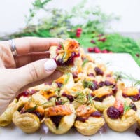 A hand holding a bitten piece of mini easy appetizer with some cranberry sauce filling and a chunk of cheese.