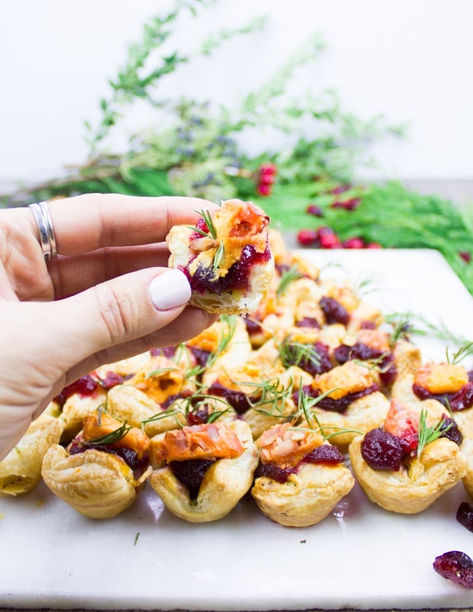 A hand holding a bitten piece of mini easy appetizer with some cranberry sauce filling and a chunk of cheese.