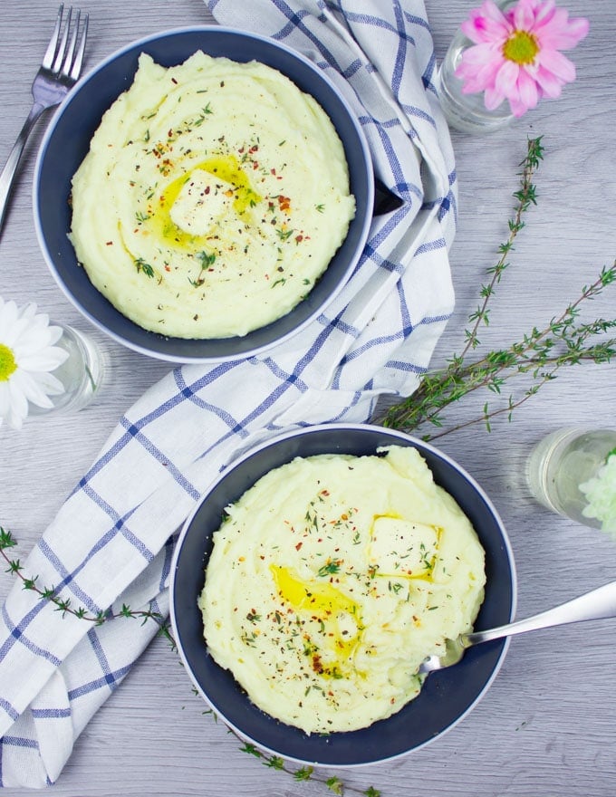 two bowls of creamy mashed potatoes with a tea towel in the middle, a small glass of flower and some green thyme leaves.