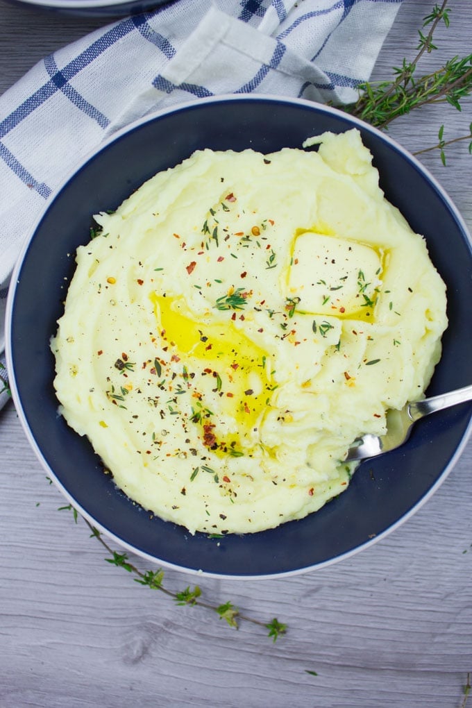 A single bowl close up of mashed potatoes and a butter in top melting, some fresh thyme leaves over it and some chilli flakes.