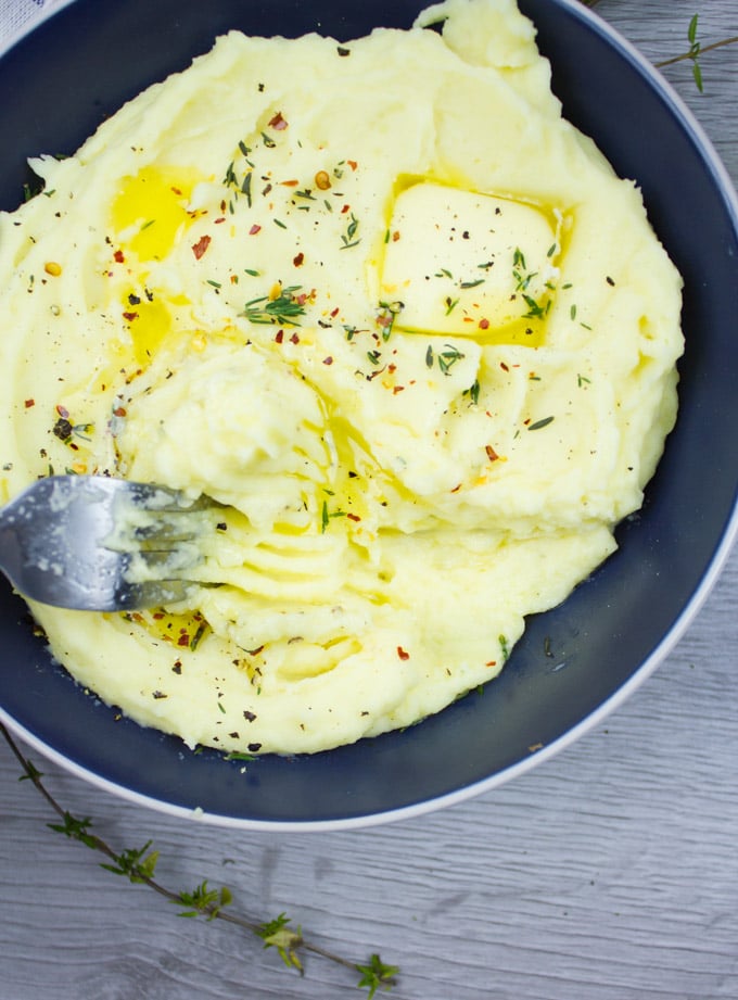 A close up bowl of mashed potatoes and a fork scraping the potatoes showing how creamy and fluffy it is.