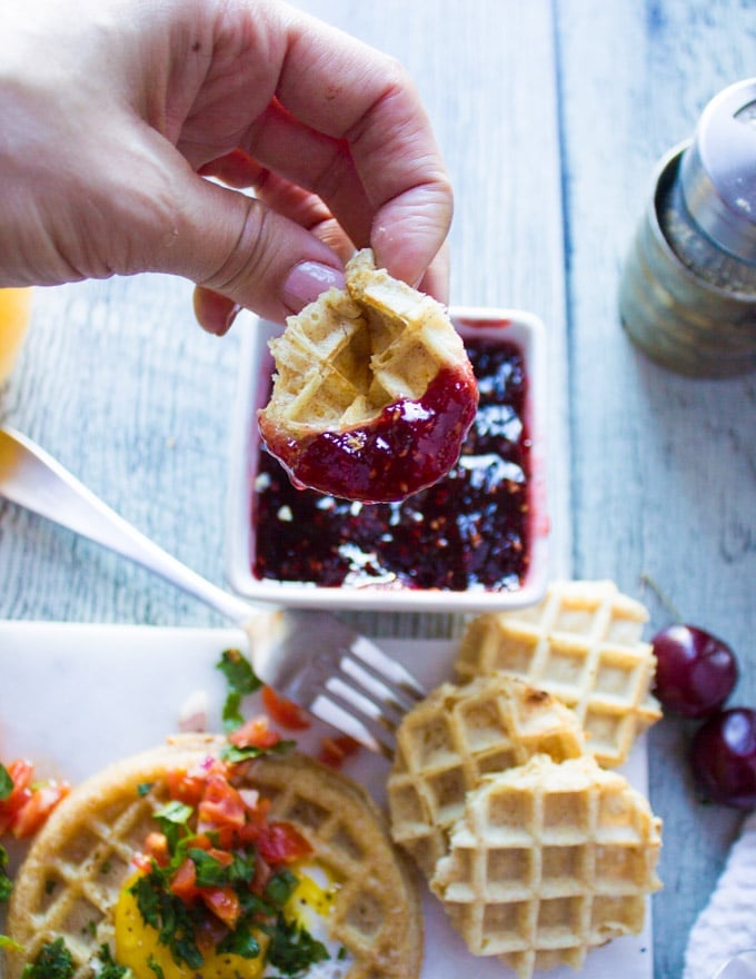 A hand holding a toasted waffle center and scooping some jam with it.