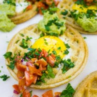 Single egg in a hole waffle up close with pico de gallo and guacamole on top.