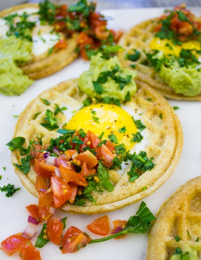 Single egg in a hole waffle up close with pico de gallo and guacamole on top.