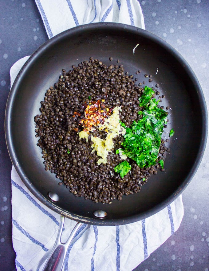 A skillet with cooked black lentils, some spicy chilli flakes, garlic and fresh parsley