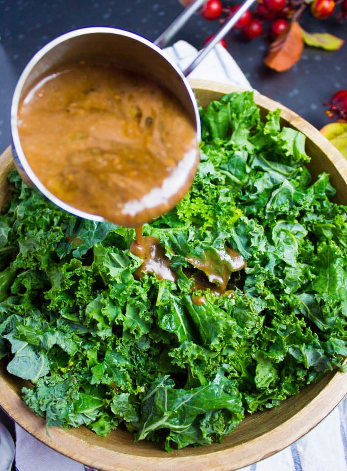 A bowl with massaged kale and a cup pouring some homemade raspberry Vinaigrette