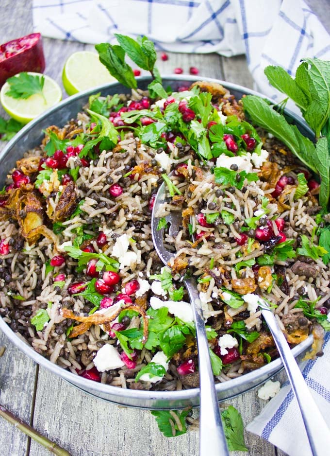 A plate of cooked Mediterranean rice and lentils aka mujadara with two spoons serving up the dish showing crispy onions and herbs on top