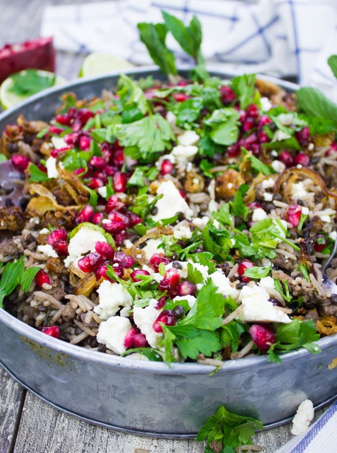 Side view of a plate of mujadara showing close up of the cooked rice and lentils and some feta cheese crumbles on top with lots of fresh herbs