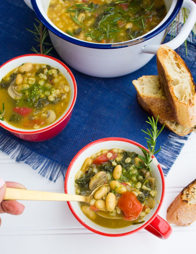 A spoon holding some soup showing white beans, chunky tomatoes and kale over a bowl of soup