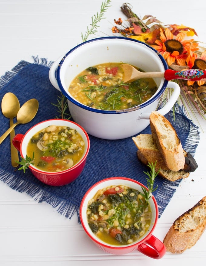 A pot of white bean soup recipe and two bowls of soups, two spoons and some crunchy bread.