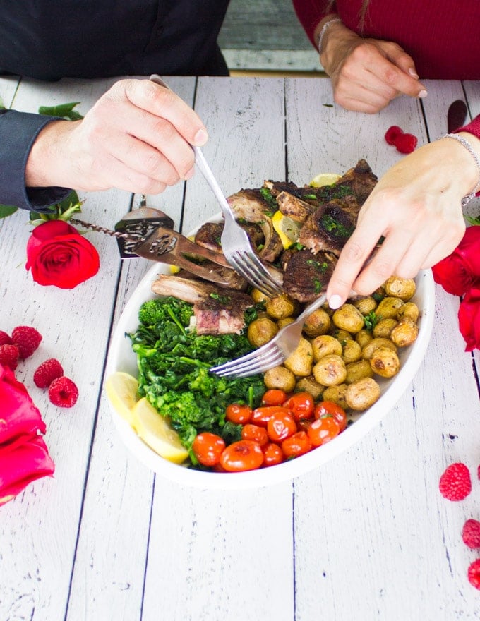 two hands holding two forks eating from the lamb chops platter together