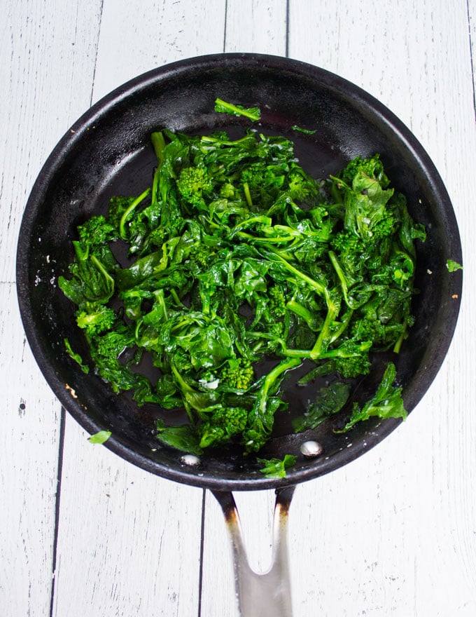 A skillet showing the broccoli rabe cooked in olive oil and garlic
