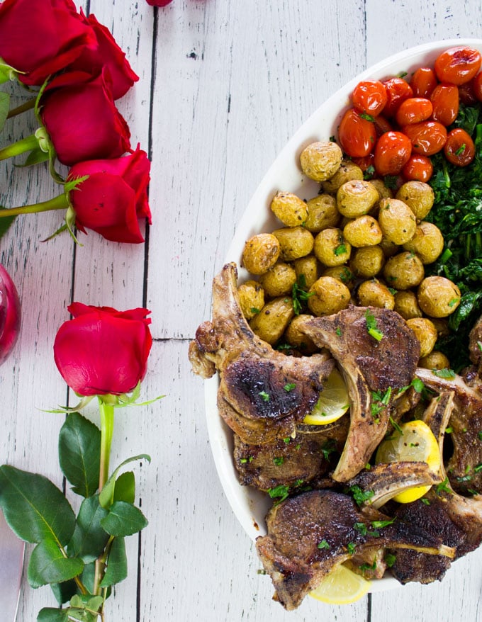 Half a platter of lamb chops on a white table with red roses