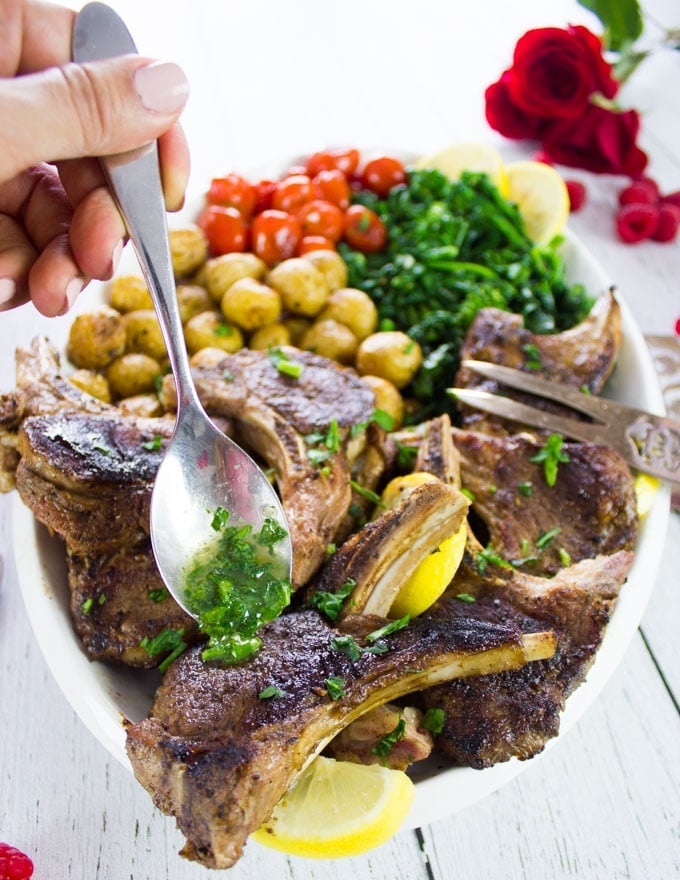 A spoon drizzling some compound herb butter over cooked lamb chops