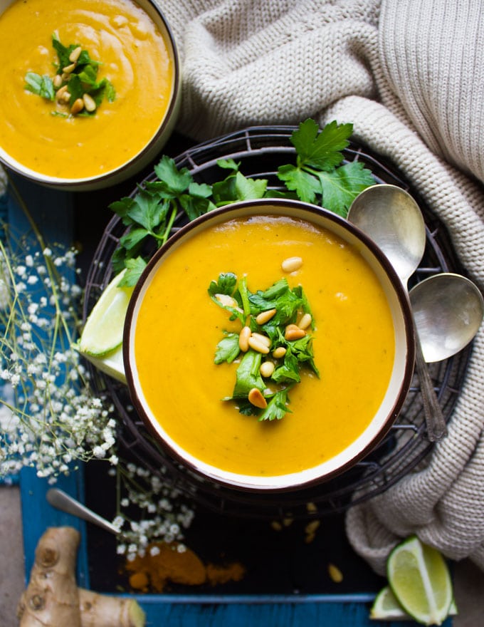A bowl of butternut squash recipe surrounded by two spoons, some lime and cilantro.