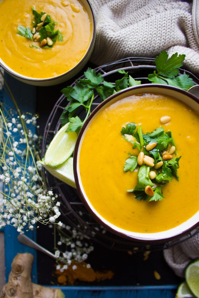 Close up of a half a bowl of vegan butternut squash soup topped with parsley and pine nuts.