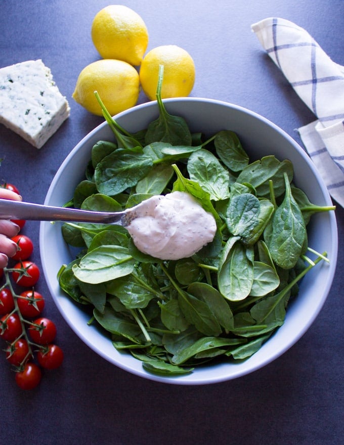 A spoon mixing blue cheese dressing over fresh greens for the salad.