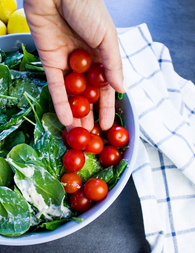 A hand pouring some cherry tomatoes to start building a smoked salmon salad.