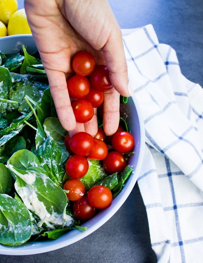 A hand pouring some cherry tomatoes to start building a smoked salmon salad.