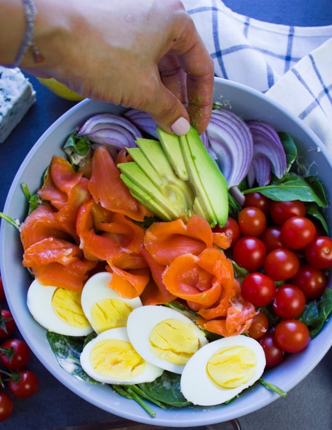 A hand arranging sliced avocados for a smoked salmon salad recipe.