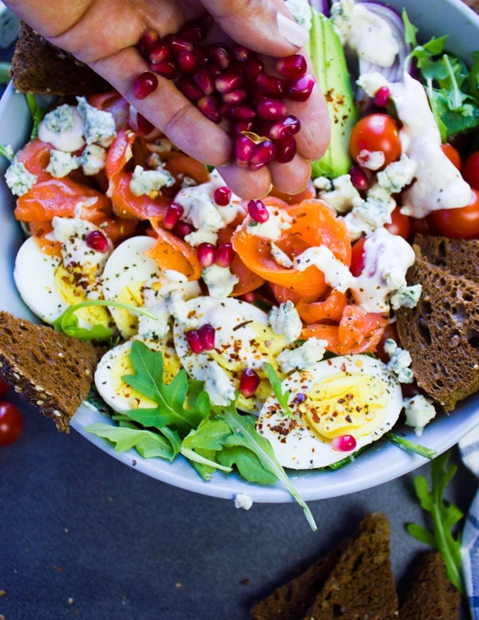 A hand sprinkling pomegranate arils over the dressed smoked salmon salad.