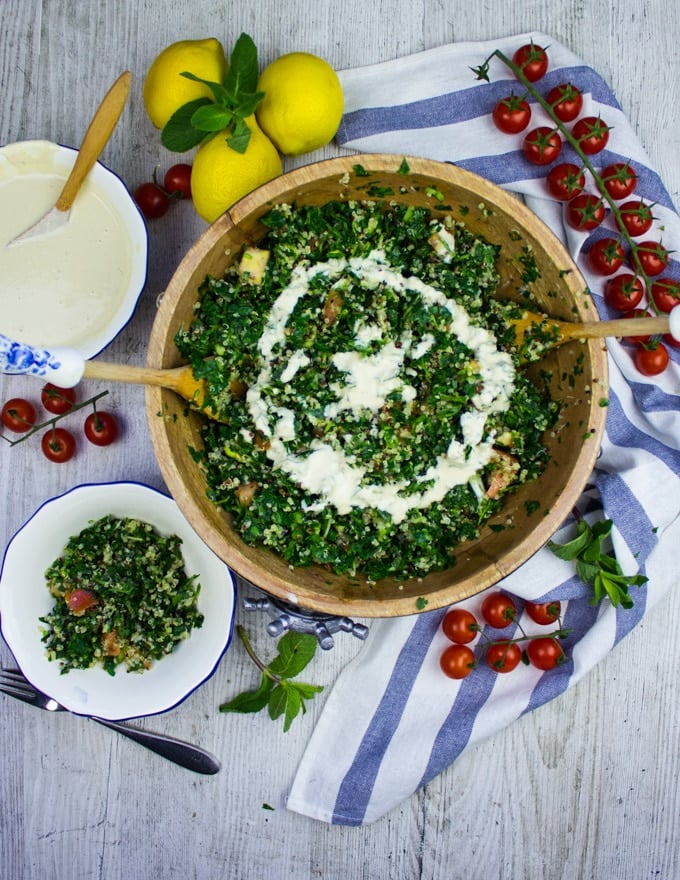 Finished tabouli salad with two serving spoons and a small plate of salad on the side 
