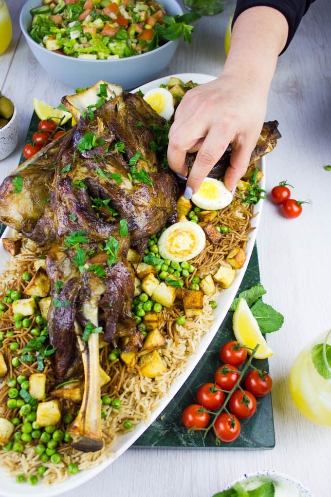 A hand arranging the hard boiled eggs on the rice all around the lamb shoulder.