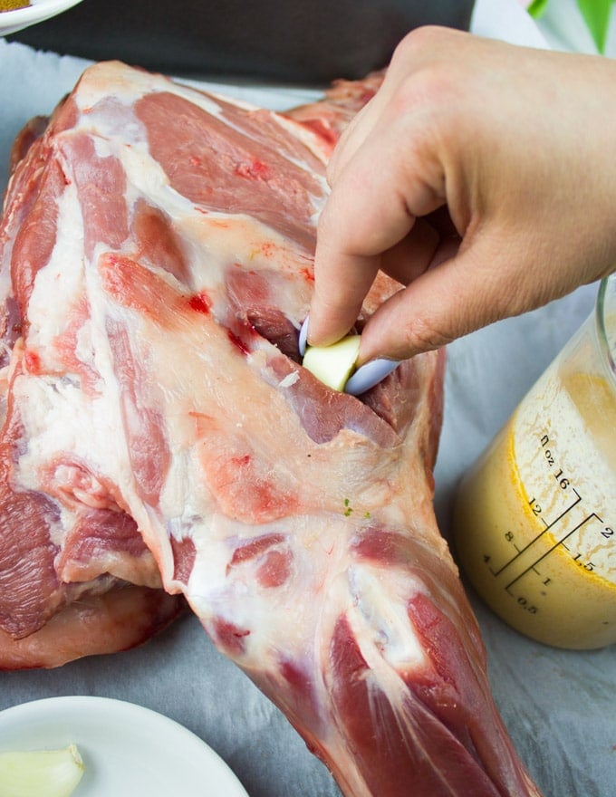 A hand inserting a garlic clove in the slits of lamb shoulder