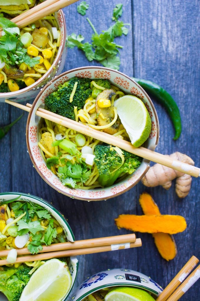 A bowl of spicy ramen with chopsticks for eating it, and turmeric root cut up with chillies around it.