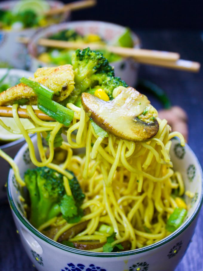Chopsticks lifting up some spicy ramen with mushrooms and broccoli.