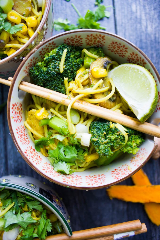 Close up of a spicy ramen bowl showing the noodles, broccoli, corn, lime wedge and chopsticks