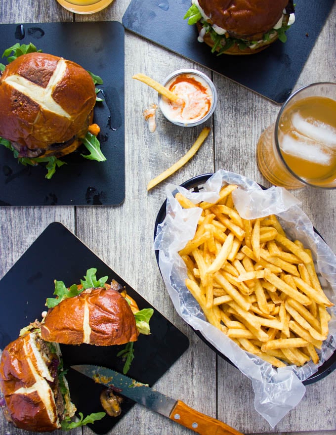 Cheese stuffed burgers on a table with one cheeseburger cut in half and some fries around it.