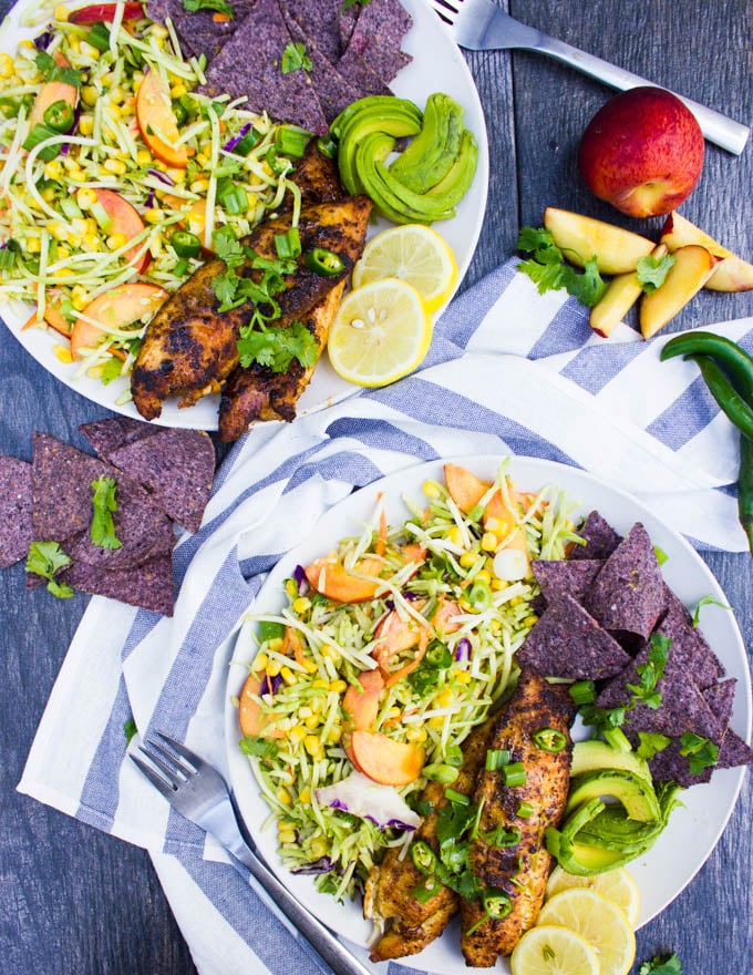 two plates of fish taco recipe with a tea towel in the middle, a peach, some green chillies, some blue corn, lemon slices