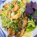 A close up of the fish taco recipe showing the taco slaw with peaches, a sliced avocado and lemon slices