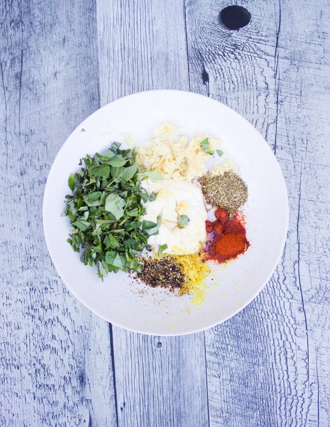 A plate of marinade ingredients for lemon chicken including mayo, lemon zest, herbs, garlic, spice