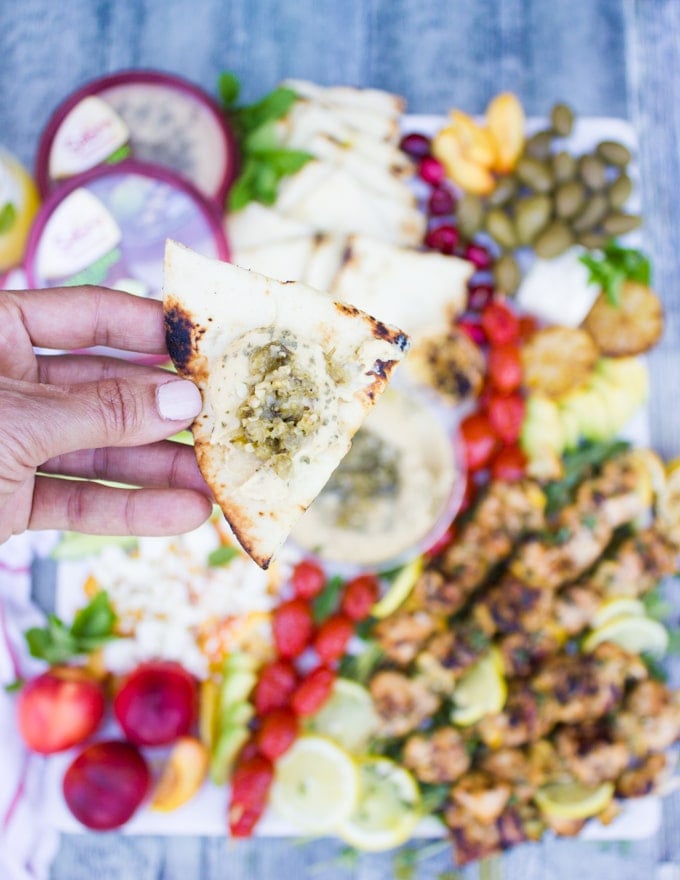 A hand holding a piece of charred bread spread with hummus