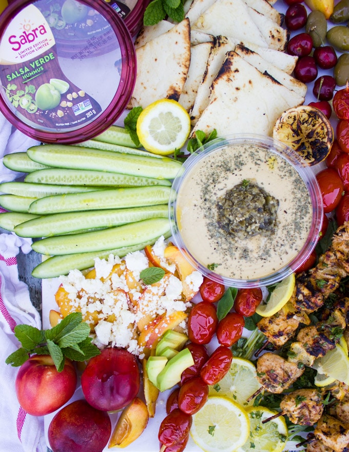 Sabra hummus box surrounded by cucumbers, peaches and grilled tomatoes
