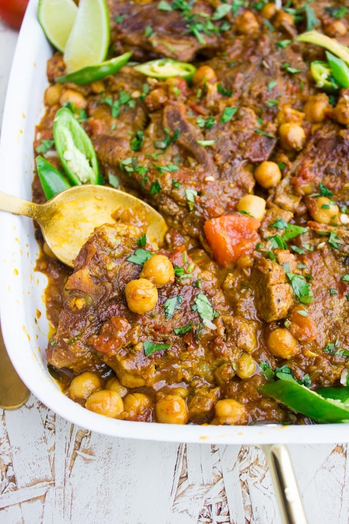 A spoon over the roast lamb and chickpeas showing close up of the tajine