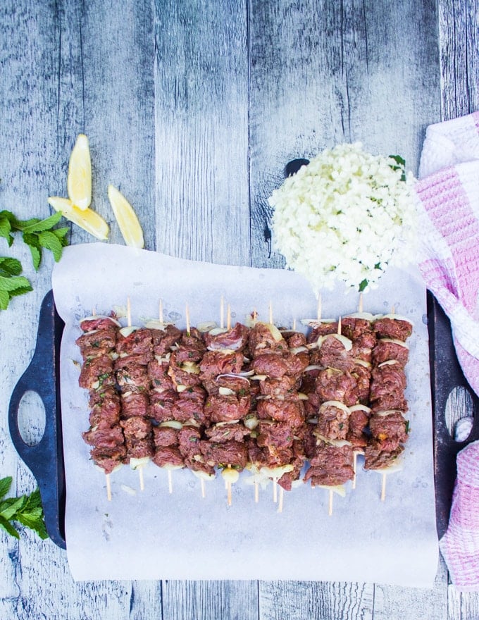 A sheet lined with paper and the skewered lamb chunks on top of it ready to be grilled