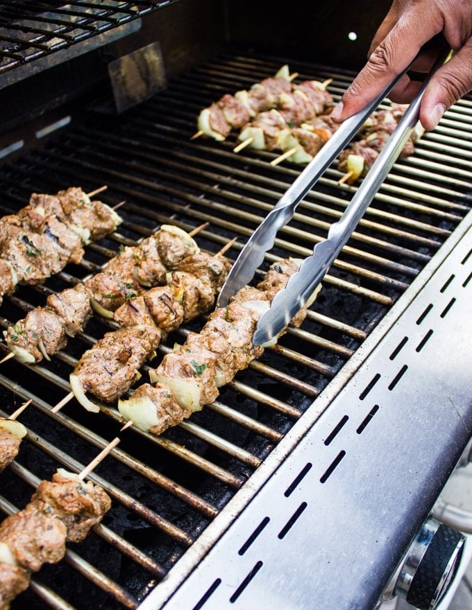 Lamb skewers on the grill and a hand holding tongs flipping them