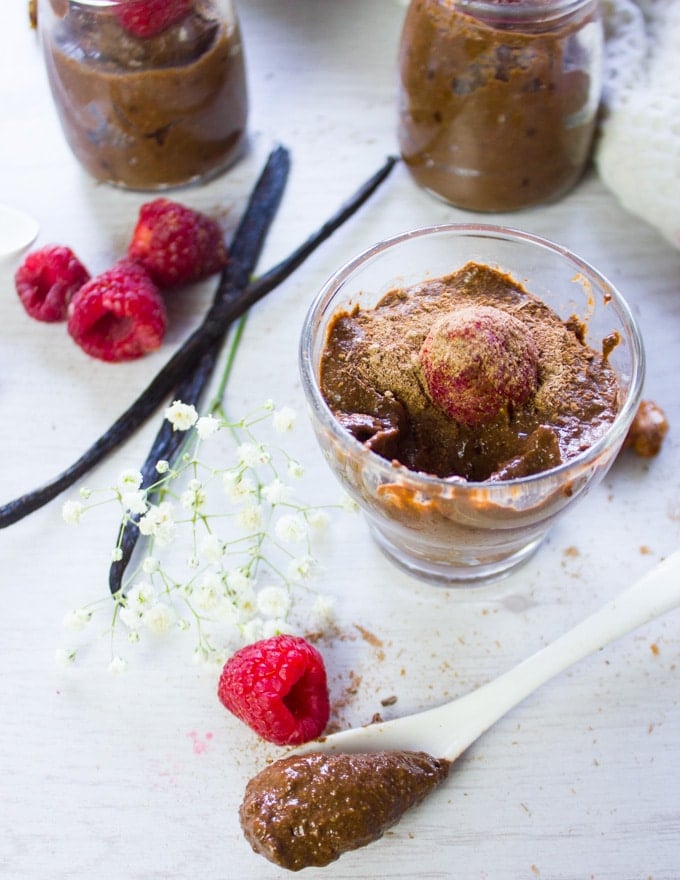 finished off scooped chocolate chia pudding in a cup and a spoon serving it with raspberries ontop for garnish