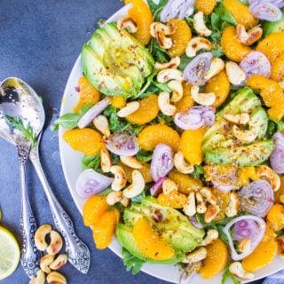 A half plate showing details of the Avocado Salad with oranges, citrus dressing, two spoons and some cashews