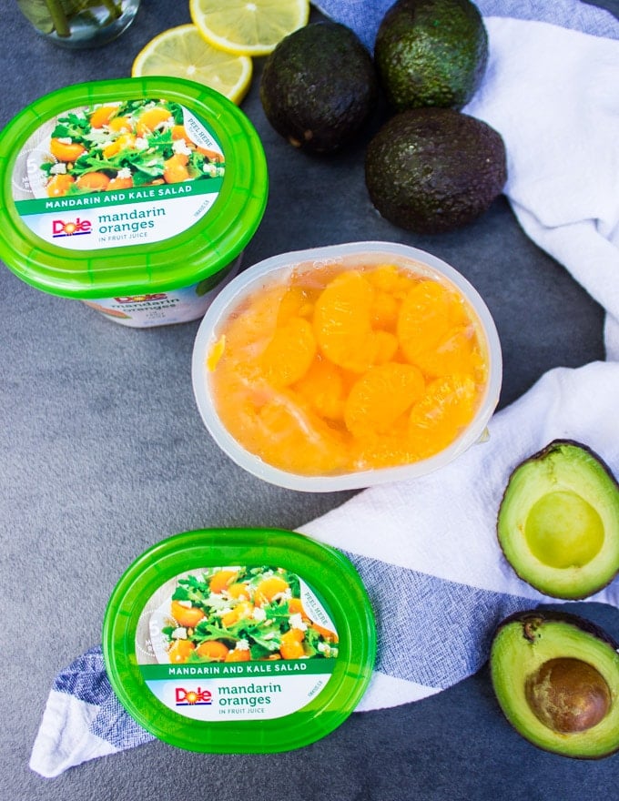 An open container showing the mandarin orange segments and surrounded by avocados to make the avocado salad