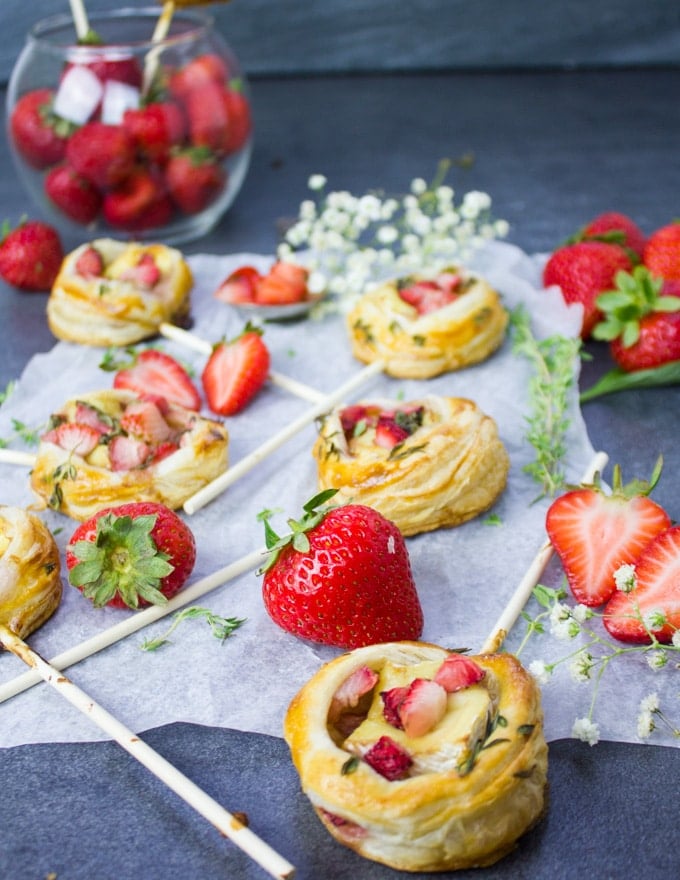 The strawberry savory hand pies piled together on a paper durrounded by fresh tsrawberries and a bowl of strawberries