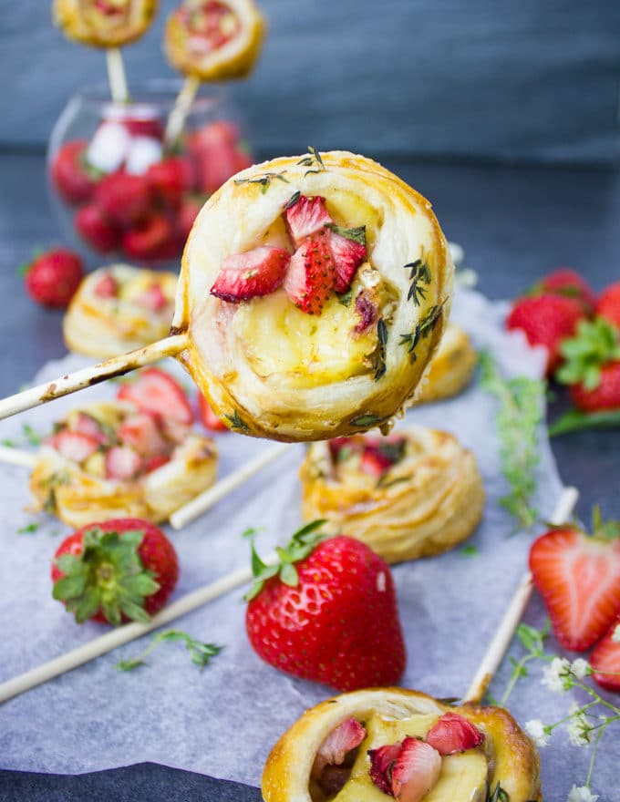 A hand holding a strawberry savory had pie on a lollipop stick close up showing the diced strawberries in the middle