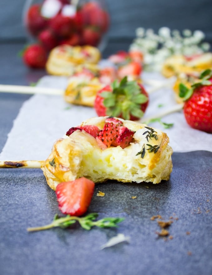 A baked hand pie on the surface bitten out to show the flakey texture, creamy brie cheese and sweet strawberries on top