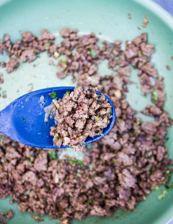 Cooked ground lamb in a pan and a spoon showing the texture