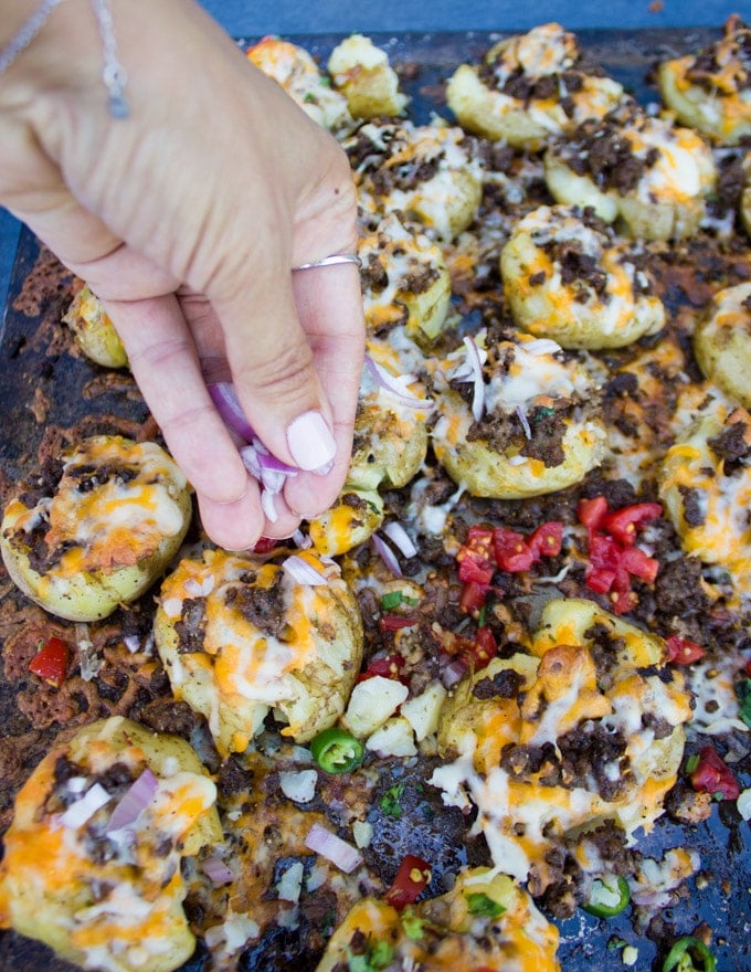 Sprinkling toppings on the smashed potatoes such as onions, tomatoes, guacamole and cilantro